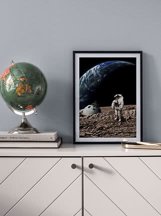Framed space poster with astronaut on rocky ground and Earth in the background on a sideboard