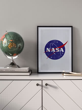Indrammet NASA-plakat på hvid kommode ved siden af en globus og bøger