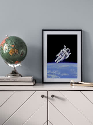 Framed astronaut poster above Earth on a white cabinet beside a globe.