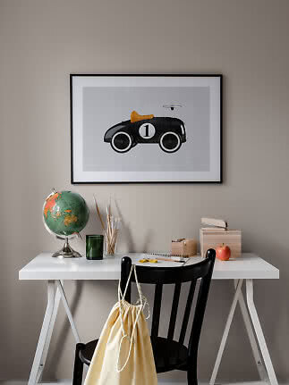 Skrivebord med globe, pensler og sort stol under indrammet plakat med sort legetøjsbil.