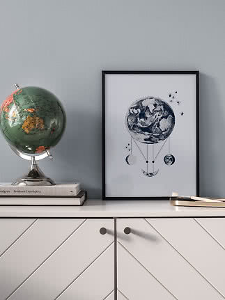 Stampa incorniciata in bianco e nero con Terra e fasi lunari su un mobile bianco accanto a un globo