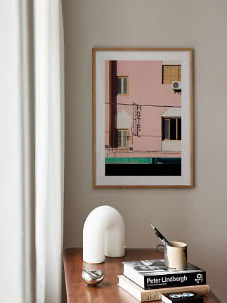Framed photo art of a pink building on a beige wall above a wooden table with books and decor