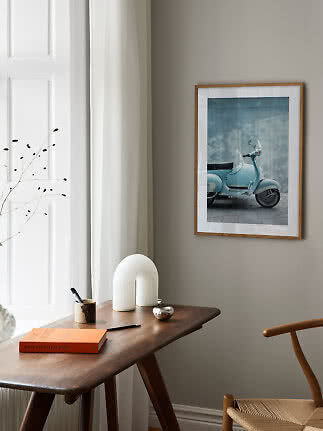 Indrammet plakat med lyseblå scooter over et træbord i et lyst, moderne rum