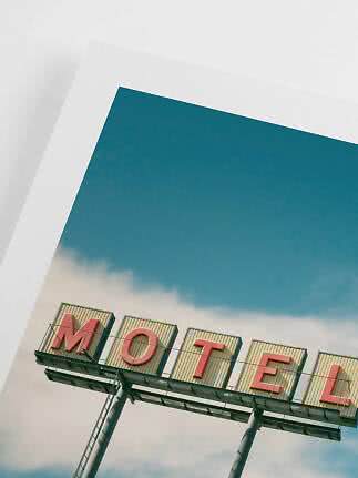 Skråt foto af et motel-skilt med røde bogstaver mod blå himmel og hvide skyer