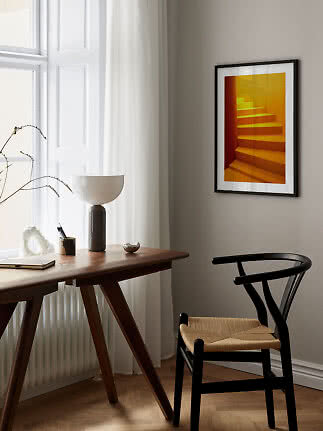 Indrammet kunsttryk med orange trappe på beige væg over skrivebord og sort stol