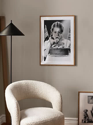 Light bouclé armchair beside a black floor lamp and framed black-and-white print on a beige wall