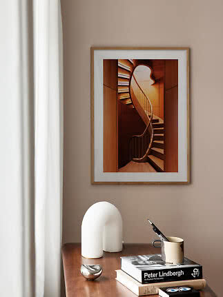 Framed art print of a curved wooden staircase above a desk with books and a mug