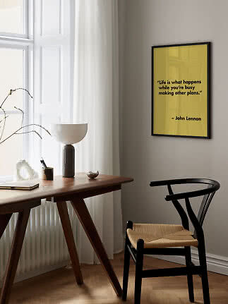 Yellow quote poster by John Lennon in black frame on wall above desk and chair