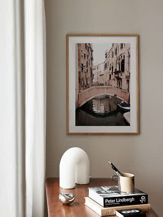 Framed canal bridge photo print above a desk with books and decorative objects