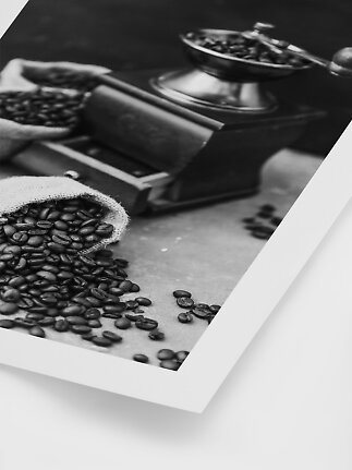 Sort-hvidt motiv af kaffebønner spildt fra en sæk ved siden af en manuel kaffekværn