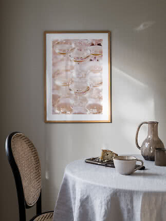 Indrammet plakat med champagneglas på væg over bord med kop, kande og kage