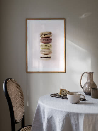 Stampa incorniciata con cinque macarons sopra un tavolo con tazza, brocca e fetta di torta.