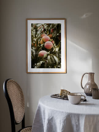Inramad bild med persikor på gren ovanför bord med kopp, kanna och kakbit.