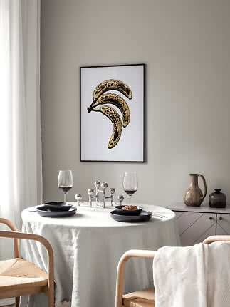 Gerahmtes Poster mit drei gesprenkelten Bananen auf weißem Hintergrund über einem Esstisch
