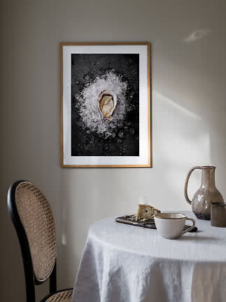 Framed art print of an oyster on crushed ice hanging above a laid dining table.