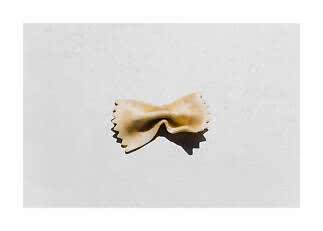 Una singola pasta farfalle su sfondo bianco con ombra netta