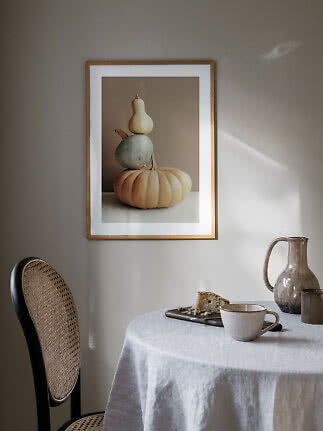 Ingelijste poster met gestapelde pompoenen op beige achtergrond boven een gedekte tafel.