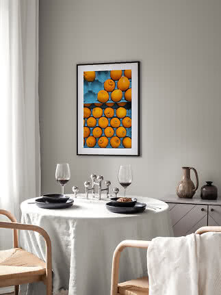 Essecke mit rundem Tisch, schwarzen Tellern, Weingläsern und gerahmtem Orangenbild an der Wand
