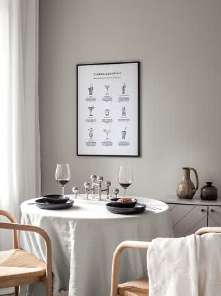 Essecke mit rundem Tisch, schwarzen Tellern, zwei Weingläsern und Cocktailposter an der Wand