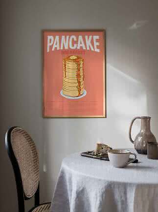 Poster incorniciato di pancake su parete sopra tavolo con tazza, brocca e fetta di torta