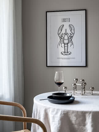 Framed lobster poster above a dining table with black tableware and a glass of red wine