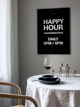 Sort plakat med teksten "Happy Hour Daily 5PM / 6PM" over et dækket bord med vinglas.