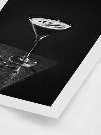 Sort-hvidt foto af cocktailglas med skummende kaffe og kaffebønner på mørk bordplade