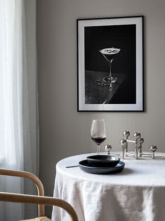 Spisehjørne med rundt bord, vinglas og indrammet sort-hvid plakat af cocktailglas