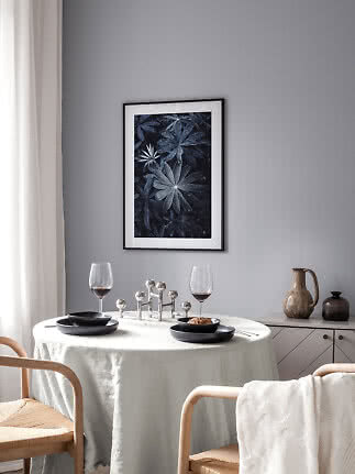 Dining area with round table, black plates, wine glasses and framed botanical print on a gray wall
