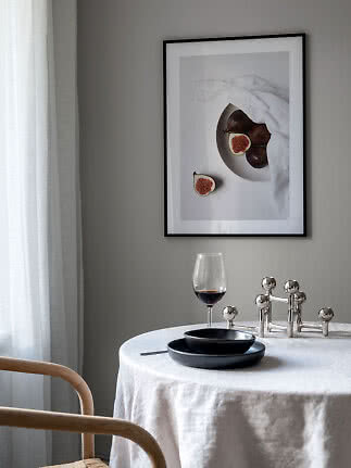 Matbord med vit duk, svarta tallrikar, vinglas och fikonbild på grå vägg