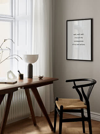 Schwarz gerahmtes Zitatposter an beiger Wand über Schreibtisch und schwarzem Stuhl im hellen Raum.