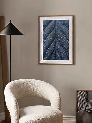 Framed poster showing a close-up of a dark leaf with water droplets on a beige wall