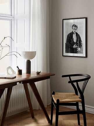 Minimalist workspace with wooden desk, black chair, table lamp, and framed black-and-white portrait.