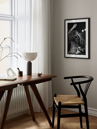 Indrammet sort-hvid koncertplakat på beige væg over skrivebord og sort stol