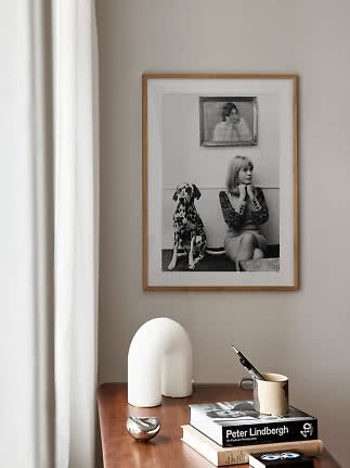 Stilrent interiør med indrammet sort-hvid foto, bøger, krus med pen og hvid skulptur på træbord