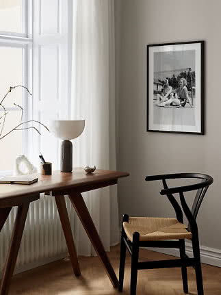 Minimalist workspace with wooden desk, black chair, table lamp, and framed black-and-white photo.