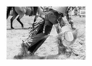 Sort-hvidt foto af cowboy, der falder i arenaen og griber sin hat, mens støv flyver op