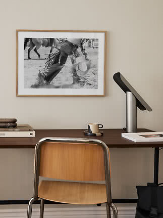Skrivebord med stol, lampe og indrammet sort-hvid cowboyfotografi på væggen
