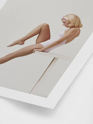 Woman in a light pink swimsuit sitting on a diving board in a minimalist white space
