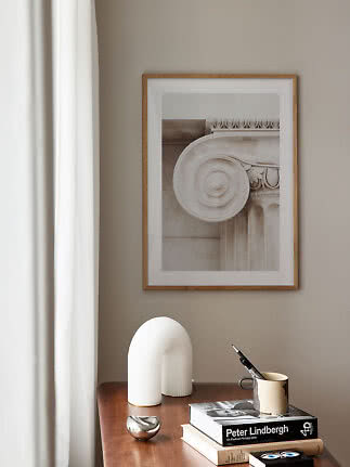 Framed art print of a classical column detail above a wooden table with books and decor