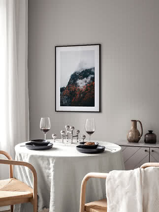 Spisehjørne med rundt bord, sorte tallerkener, vinglas og indrammet bjergplakat på grå væg