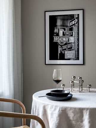 Indrammet sort-hvid plakat med gadeskilte over et dækket bord med vinglas og sorte tallerkener