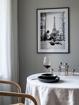 Spisebord med hvid dug, sorte tallerkener og vinglas under indrammet sort-hvid Paris-plakat