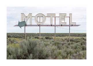 Grande insegna vintage di motel con freccia in un paesaggio di arbusti sotto cielo nuvoloso