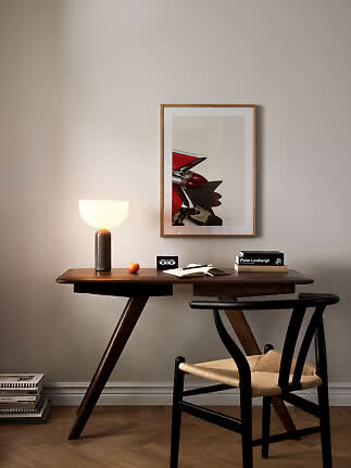 Wooden desk with black chair, glowing table lamp, books, and framed car photo on the wall