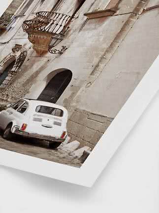 White vintage car parked beside an old stone building with a wrought-iron balcony.
