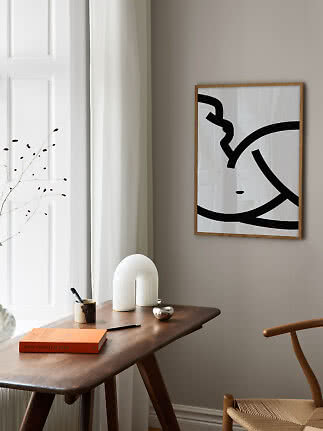 Gerahmter abstrakter Schwarz-Weiß-Druck über einem Holztisch in einem hellen minimalistischen Raum