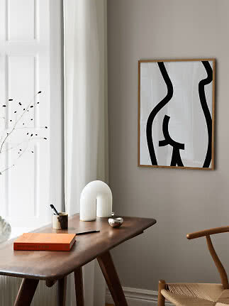 Abstract black and white poster in a light wood frame above a wooden desk in a bright minimalist room