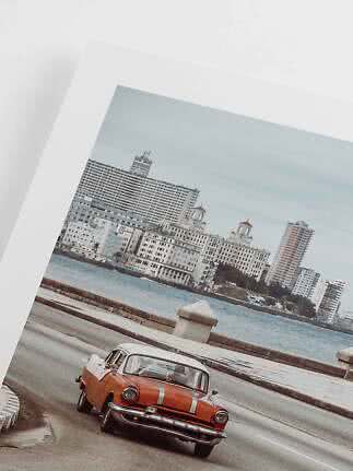 Framed photo of an orange vintage car on a coastal road with city and water behind