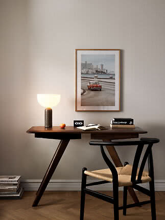 Dark wooden desk with lit table lamp, chair, and framed car photo on the wall